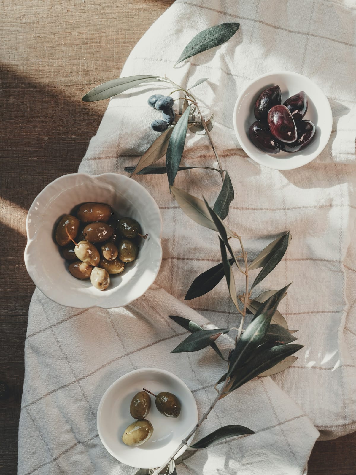 Keten örtü üzerinde zeytin dolu küçük kâseler ve bir zeytin dalı